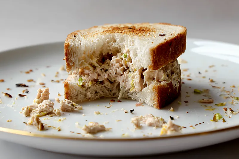 A lonely tuna sandwich on a plate, half-eaten, symbolizing the awkward reality of grief