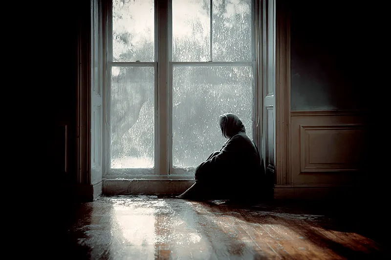 A single figure sitting by a rain-streaked window, soft light casting long shadows, symbolizing the quiet ache of loneliness